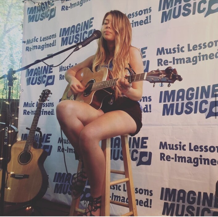 An Imagine Music student singing and playing guitar at a recital in Ogden